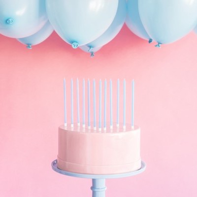 Bolo rosa com velas azuis frente a uma parede rosa e balões azuis