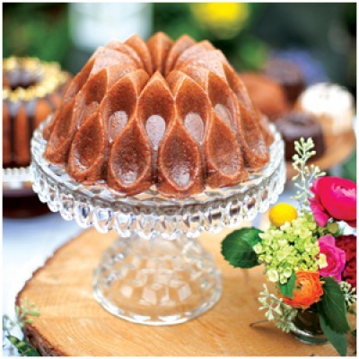 Bolo dourado com design decorativo em suporte de vidro e arranjo floral ao lado