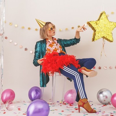 Mulher festiva com roupa colorida sentada rodeada de balões e estrelas decorativas