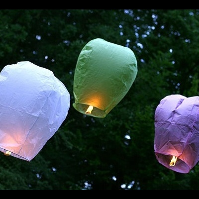 Três lanternas flutuantes de papel em branco, verde claro e lilás acesas ao ar livre