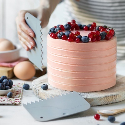 Bolo rosa decorado com frutos vermelhos e mirtilos com espátulas cinza e ovos ao fundo