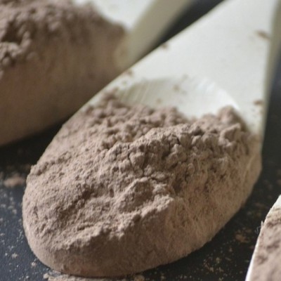 Colher branca cheia de pó castanho sobre superfície escura