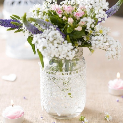 Vaso de vidro com renda branca e arranjo de flores frescas sobre mesa com velas