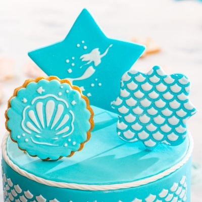 Bolo azul claro decorado com padrão de escamas e bolachas decorativas azuis e brancas