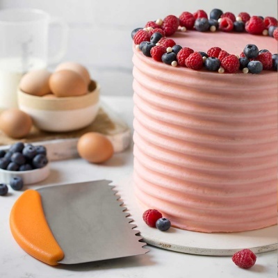 Bolo rosa decorado com frutas vermelhas e uma espátula com cabo laranja ao lado