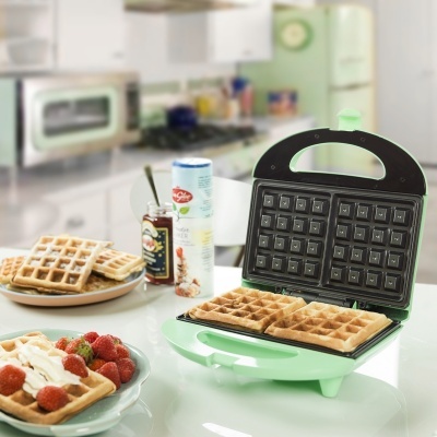 Forno eléctrico verde para waffles com waffles dourados e ingredientes em cozinha moderna