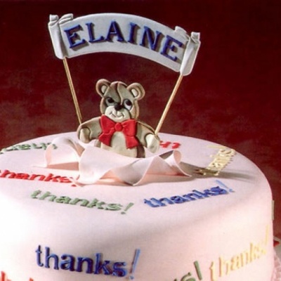 Bolo branco decorado com textos 'thanks!' coloridos e urso com faixa 'ELAINE'