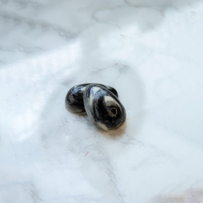 Duas pedras lisas pretas e cinzentas com furos no centro sobre mármore branco