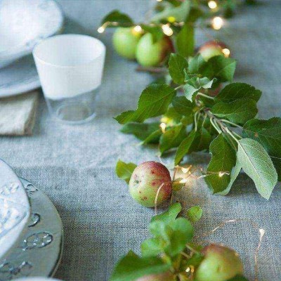 Ramos com maçãs verdes e vermelhas decorados com luzes de fada sobre superfície cinza