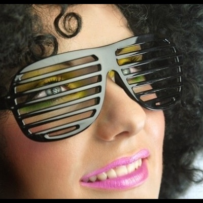 Óculos escuros pretos com ripas horizontais usados por pessoa com cabelo encaracolado e batom rosa