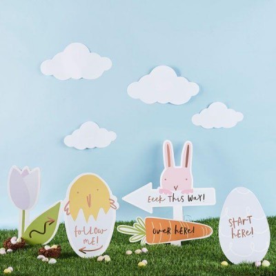 Placas decorativas coloridas em formato de animais e objetos da Páscoa sobre relva artificial com fundo azul e nuvens de papel