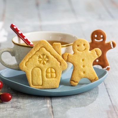 Biscoitos decorativos em forma de casa e boneco de gengibre num prato azul com uma caneca ao fundo
