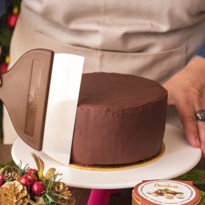 bolo coberto com chocolate num prato branco com decoração natalícia e embalagem Decora ao lado