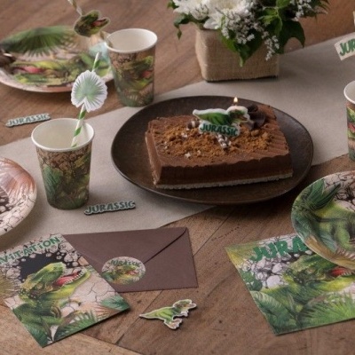 Mesa decorada com pratos e copos de papel com tema de dinossauros, bolo quadrado e etiquetas com os textos JURASSIC e JURASSIC WORLD