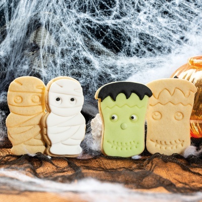 Bolachas decoradas de Halloween com múmias e Frankenstein sobre fundo com teias de aranha e abóbora.