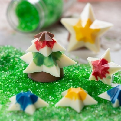 Mini árvore de Natal e estrelas de chocolate coloridas em cima de grânulos verdes