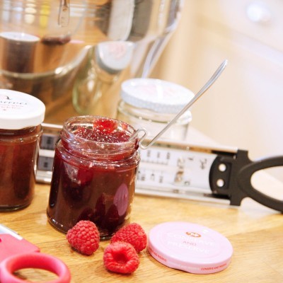 Frasco aberto de compota vermelha com colher e framboesas frescas