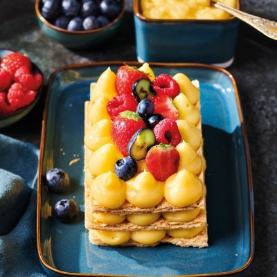 Tarte rectangular com creme amarelo e frutos vermelhos num prato azul