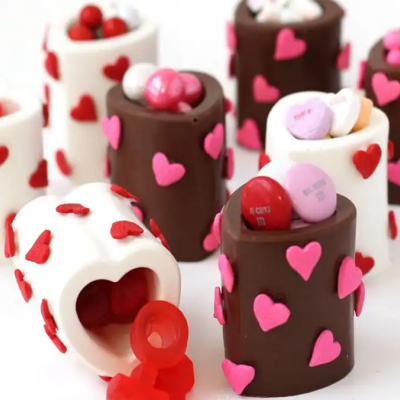 Recipientes de chocolate decorados com corações contendo balas coloridas.