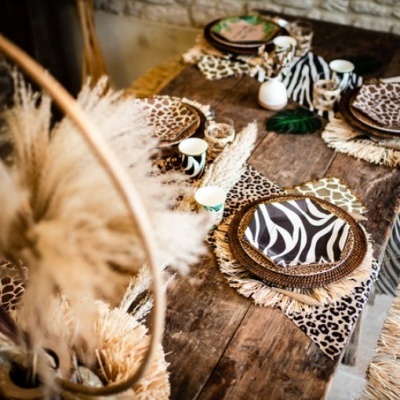 Mesa de madeira com decoração animal print zebras e leopardos com pratos, copos e garrafas de cerâmica