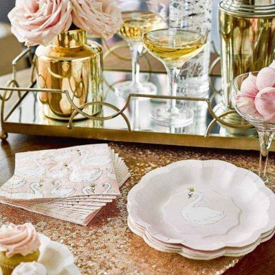 Pratos e guardanapos com cisne, taças com bebida, vaso dourado com flores