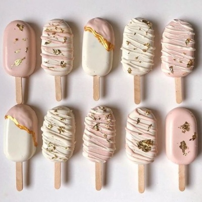 Dez gelados em pauzinho com cobertura em rosa, branco e bege, decorados com detalhes dourados e listras.