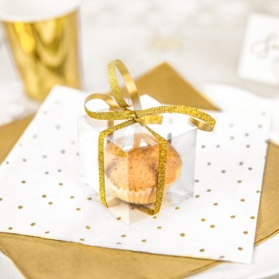 Caixa transparente com bolo pequeno e fita dourada sobre guardanapos e prato branco