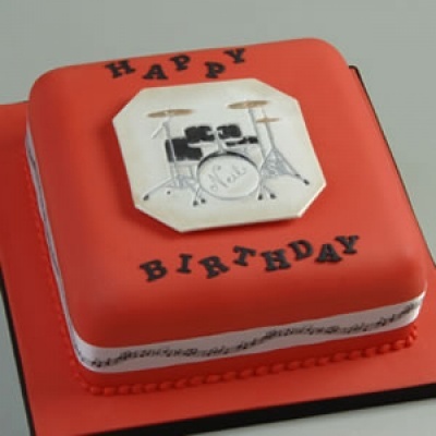 Bolo quadrado vermelho com decoração de bateria e texto 'HAPPY BIRTHDAY'