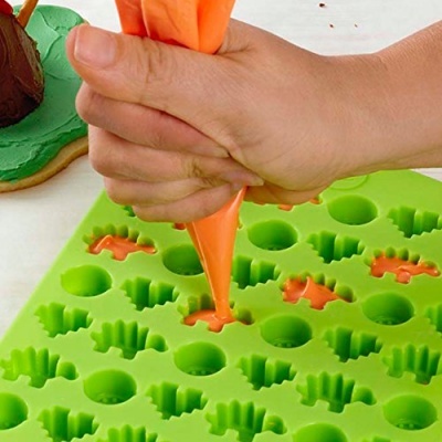 Molde de silicone verde com cavidades de dinossauros e ossos preenchido com creme laranja com saco de pasteleiro
