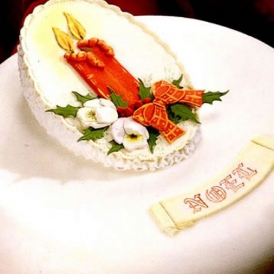 Bolo branco decorado com velas, azevinho, flores e palavra NOEL