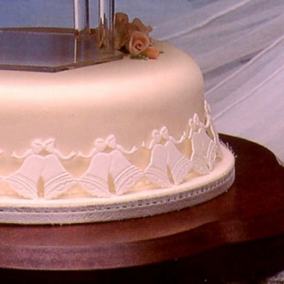 Bolo redondo branco com decoração de sinos e flores no topo