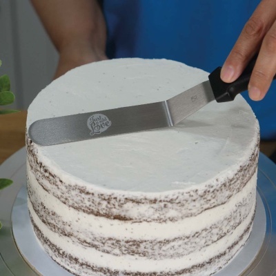 Bolo redondo com creme branco a ser alisado por espátula metálica com texto Funky Love