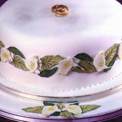 Bolo branco decorado com flores e folhas em pasta americana e anéis dourados no topo