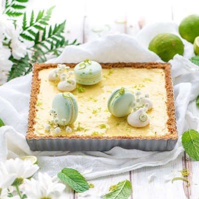 Tarte quadrada com recheio amarelo e decoração de macarons verdes claros e flores brancas