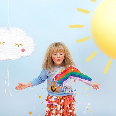 Criança com roupa colorida a brincar com confetes e balões de nuvem e sol