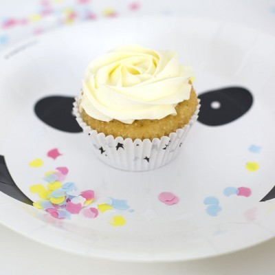 Cupcake com cobertura branca num prato com rosto de panda e confetes coloridos