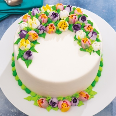 Bolo redondo branco decorado com flores de glacê coloridas e folhas verdes