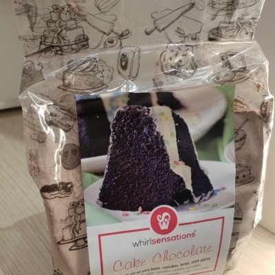 Pacote de mistura para bolo de chocolate Whirlsensations com imagem de bolo e utensílios de cozinha desenhados ao fundo