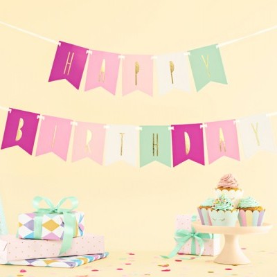 Decoração de festa com faixas 'HAPPY BIRTHDAY', presentes embrulhados e cupcakes coloridos sobre mesa clara.