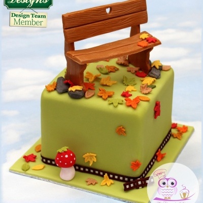 Bolo verde decorado com banco de madeira, folhas coloridas e cogumelo em miniatura