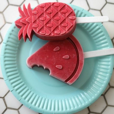 Dois gelados vermelhos em forma de abacaxi e morango sobre prato azul claro