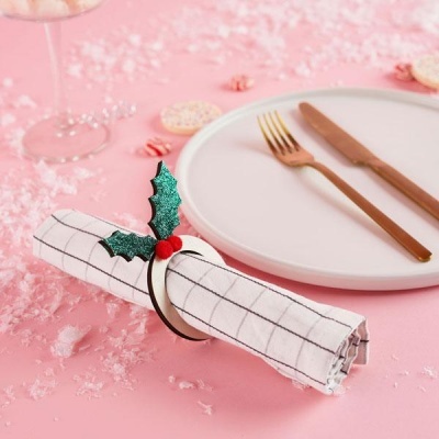 Guardanapo branco com padrão de grelha e porta-guardanapo decorado numa mesa rosa com prato branco e talheres dourados