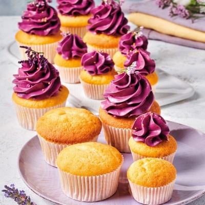 Doze cupcakes com cobertura roxa e decoração floral em pratos lilás sobre fundo claro
