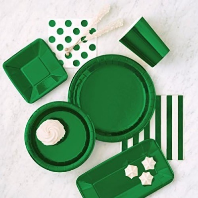 Conjunto de loiça descartável verde com guardanapos às riscas e bolinhas, e doce branco sobre prato num fundo mármore