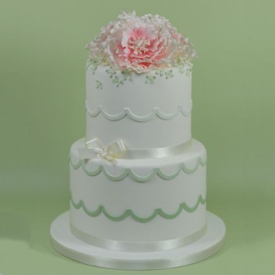 Bolo branco de dois andares com decoração verde, laço e flor rosa no topo