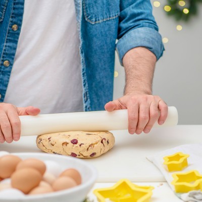 Homem a enrolar massa com rolo de massa branco perto de ovos e cortadores de estrela amarelos
