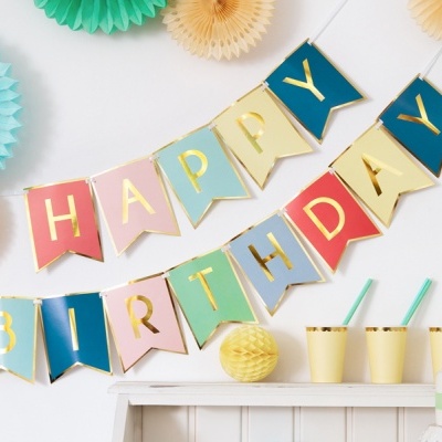 Bandeirolas coloridas com texto HAPPY BIRTHDAY, copos amarelos e enfeites de papel em fundo branco