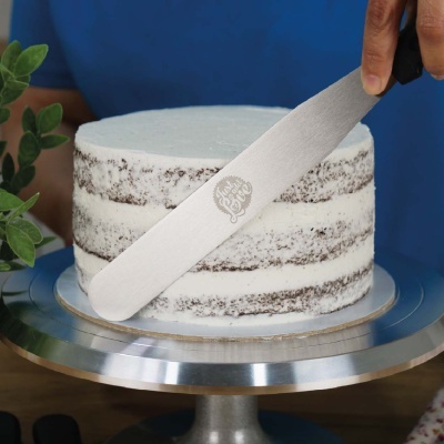 Bolo semi-naked com cobertura branca numa base metálica com mão segurando espátula