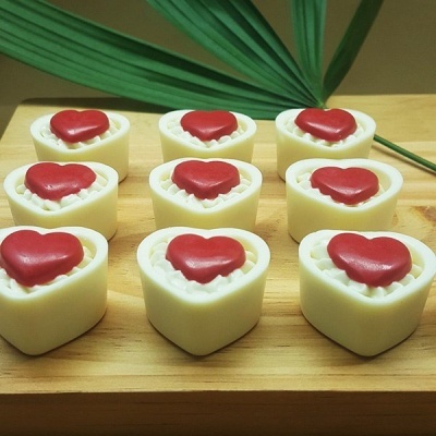 Velas em forma de coração branco com corações vermelhos no topo, sobre tábua de madeira com folha verde