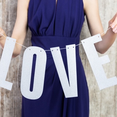 Pessoa com vestido azul segura letras brancas LOVE em fundo de madeira